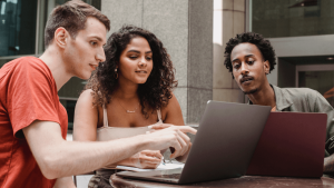 Three diverse professionals collaborating on customer relationship strategies with laptops at an outdoor café.