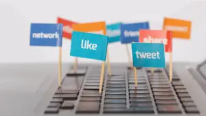 Small flags with social media terms like 'like,' 'share,' and 'tweet' inserted into a laptop keyboard, symbolizing how social media actions boost SEO and digital marketing results.