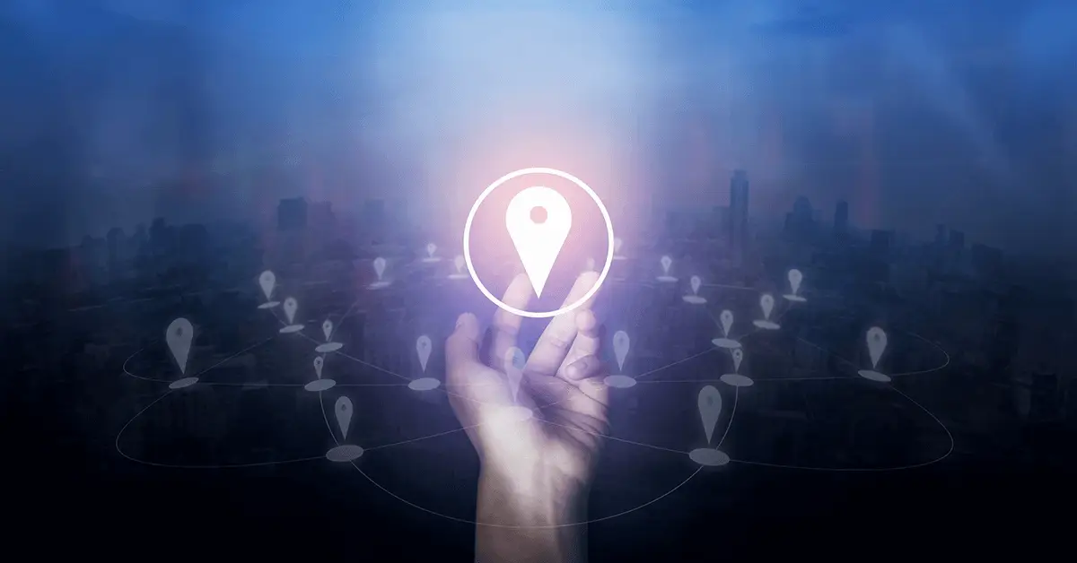 Hand reaching up to a glowing location pin with a city skyline backdrop, connected by network lines.