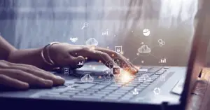 A person's hands typing on a laptop, with a glowing AI chip graphic overlaid and surrounded by cloud and data icons.