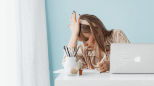 A woman at her desk looking frustrated and overwhelmed with a hand on her forehead while working on a laptop, representing the stress of managing an outdated or underperforming business website.